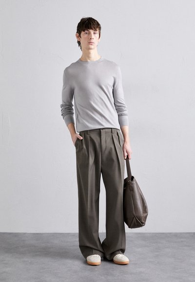 Pull gris ajusté à manches longues associé à un pantalon ample vert olive. Le mannequin porte un sac en cuir marron. Baskets blanches avec semelles beige.