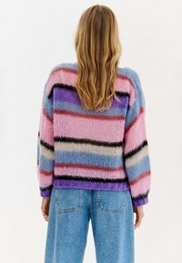 Pletený svetr s živými pruhy v růžové, modré a černé barvě. Má měkký, texturovaný povrch a volný střih, doplněný o kalhoty s vysokým pasem.