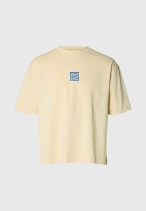 Bézs rövid ujjú póló, amelyen a mellkason középen egy kis kék négyzet alakú logó található, „Grand Amour Hotel” felirattal.