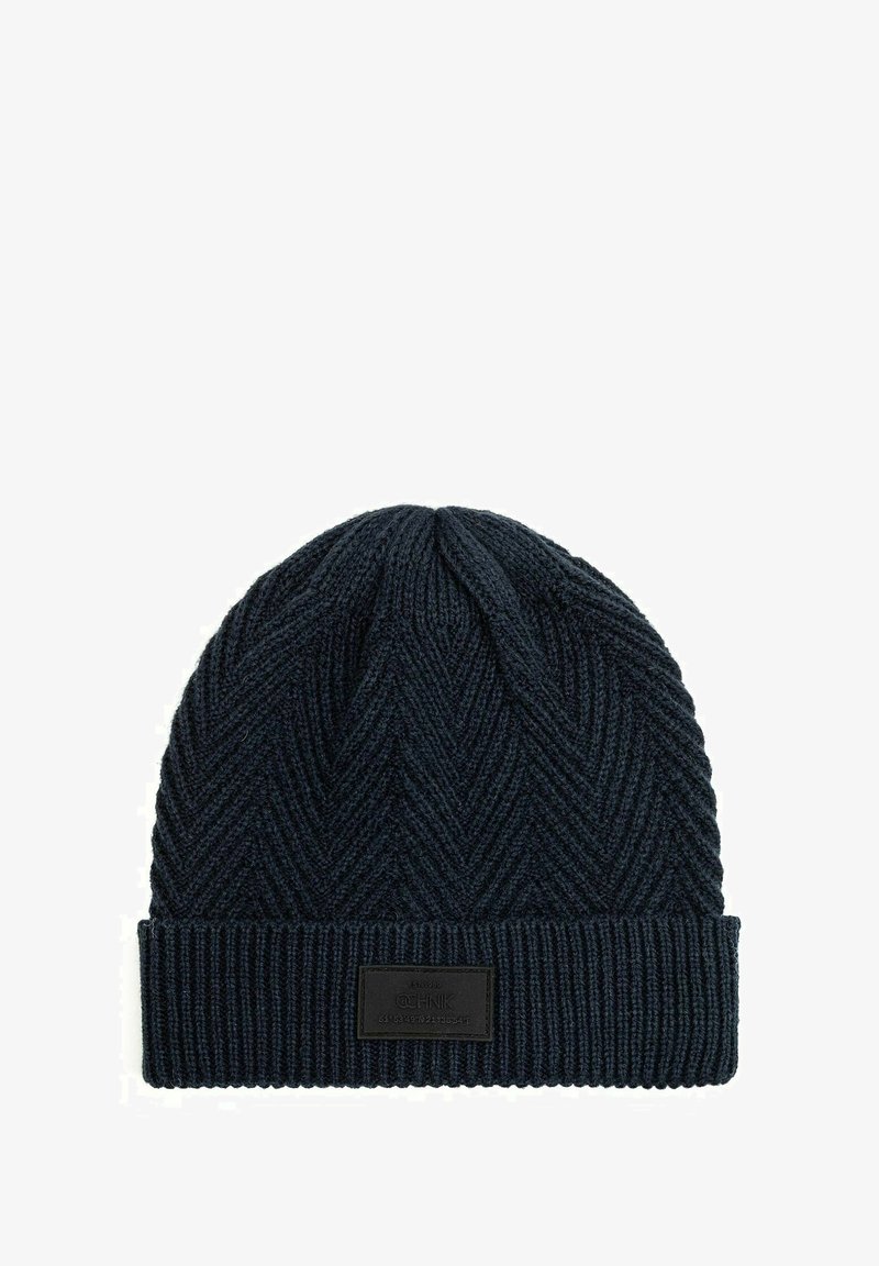 Dzianinowa czapka w ciemnoniebieskim kolorze z deseniem w jodełkę oraz prążkowanym mankietem. Posiada prostokątną łatę z logo z przodu.