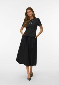 Czarny zestaw składający się z bluzki z krótkim rękawem z dekoltem w kształcie łezki i dwoma kokardkami, połączonej z zwiewną, czarną maxi spódnicą. Tkanina o fakturze.