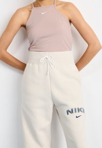 Sportovní podprsenka Nike v světle růžové barvě s tenk ými ramínky, doplněná krémovými tepláky s vyšitým námořnickým logem "NIKE" a šňůrkovým pasem.