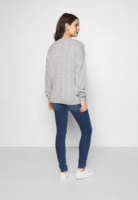 Suéter cinza de malha com mangas longas, apresentando um decote e uma bainha canelados, emparelhado com jeans skinny azul escuro e sapatilhas brancas.