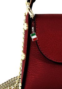 Rode leren handtas met gouden kettingriem, voorzien van een drukknoopsluiting en een klein charm van de Italiaanse vlag eraan bevestigd. Textuur oppervlak met fijne stiksels.