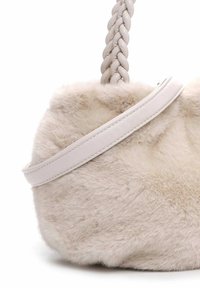 Zacht beigem colffaux-bont handtas met gevlochten handvat en glad leren schouderband tegen een witte achtergrond.