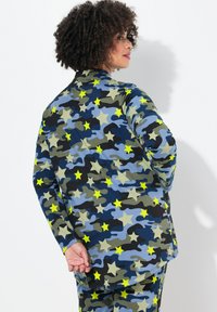 Långärmad topp i blått, grönt och svart kamouflage-mönster med gula stjärnor. Mjuk material med avslappnad passform, rund halsringning och böjd fåll.