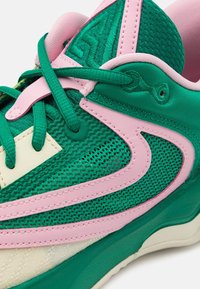 Chaussure de sport verte et rose avec tissu en mesh, accents texturés, lacets plats et design multi-couches avec une semelle arrondie.