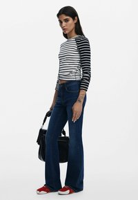 Gestreiftes Langarmoberteil mit schwarz-weißem Muster, kombiniert mit blauen Flared-Jeans und roten Sneakers. Trägt eine schwarze Handtasche.