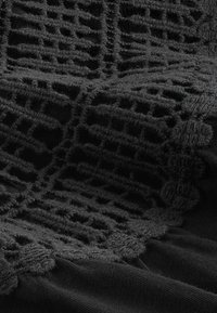 Černá látka s texturovanými, vyvýšenými vzory s mřížkovým designem a vroubkovanými okraji. Jemná textura s matným povrchem.