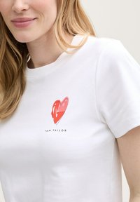 Bílá bavlněná tričko s červeným srdcem a logem "TOM TAILOR" pod ním. Krátké rukávy a kulatý výstřih. Měkká textura.