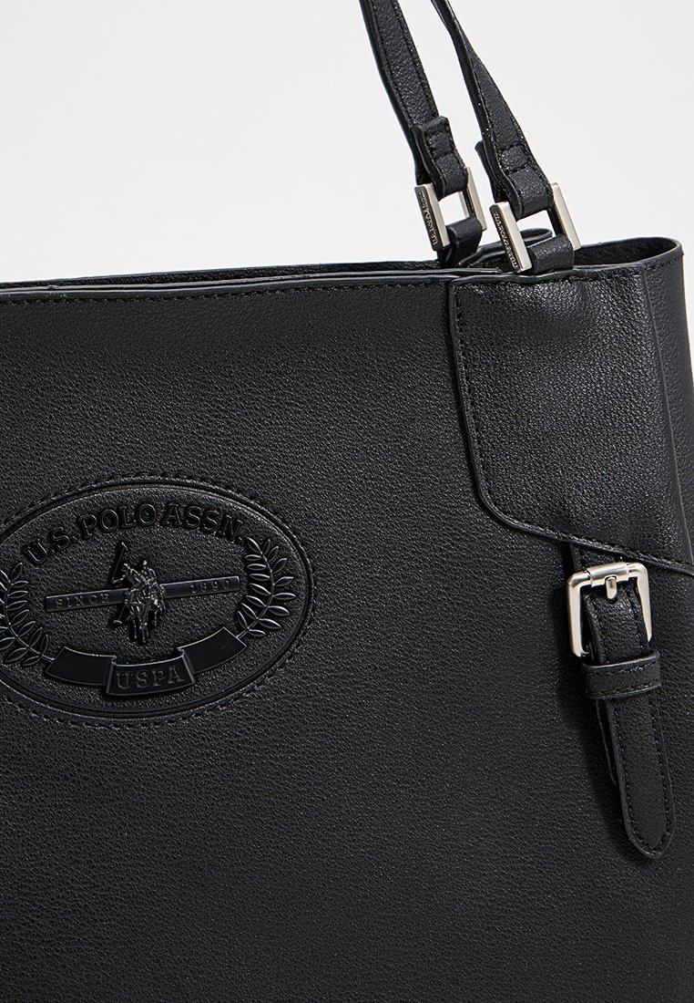 Schwarze Handtasche aus synthetischem Leder mit verstellbaren Trägern, ausgestattet mit einer strukturierten Oberfläche und einem auffälligen geprägten U.S. Polo Assn. Logo.