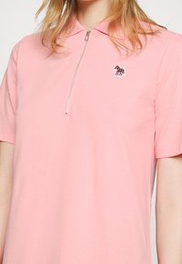 T-shirt polo rose en coton, avec une demi-fermeture éclair et un petit logo de cheval brodé sur la poitrine gauche. Manches courtes et col classique.