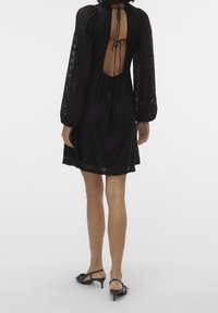 Svart spetsklänning med puffärmar och djup ryggöppning, med dragsko i midjan och längd ovanför knäna. Strukturerad tyg och delikata detaljer.
