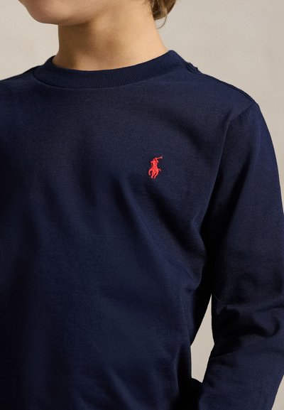 Barn iført en marineblå langærmet skjorte med en lille rød broderet polo-spiller logo på brystet.
