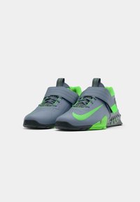 Sapatos desportivos com parte superior cinza e detalhes em verde, apresentando uma tira sobre os atacadores, sola de borracha texturizada e detalhes perfurados.
