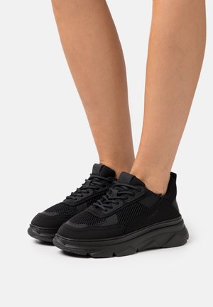 Baskets de sport noires avec dessus en mesh et synthétique, semelle épaisse texturée, bout rond et système de laçage pour un maintien sûr.
