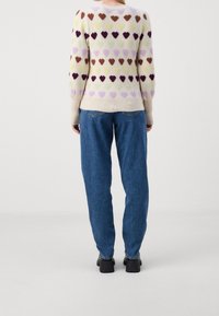 Pull en mélange de laine avec motifs de cœurs multicolores en beige, associé à un jean denim bleu clair et des chaussures noires à talons.