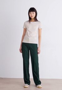 Chemise à manches courtes rayée beige avec des rayures brun clair, associée à un pantalon droit vert taille haute et des baskets blanches.
