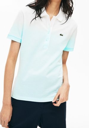 Kvinde iført en lyseblå kortærmet poloshirt med krave og knapper, kombineret med mørkeblå shorts.