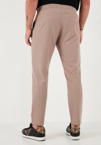 Lichtbeige broeken met een elastische tailleband, slim fit en een achterzak, gecombineerd met zwart-gouden sneakers met een logo.