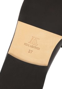 Black leather shoe sole with a beige insole. Stamped engravings read "KS REAL LEATHER" and size "37." Smooth texture with a rounded shape.