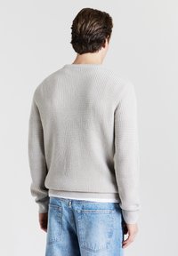 Hellgrauer strukturierter Pullover mit Rundhalsausschnitt und gerippten Bündchen. Kombiniert mit hellblauen Jeans im lässigen Schnitt und einer Tasche auf der Rückseite.