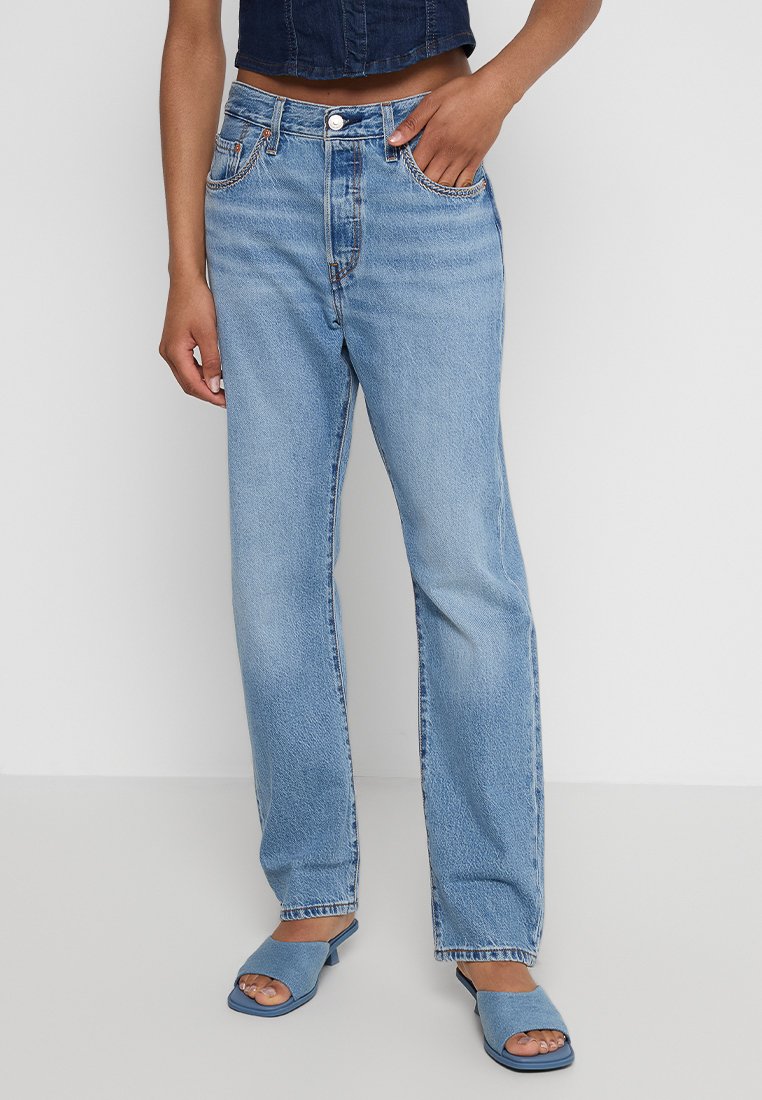 Jeans in denim azzurro chiaro con vita alta, taglio dritto e cuciture visibili. Abbinati a scarpe aperte blu.
