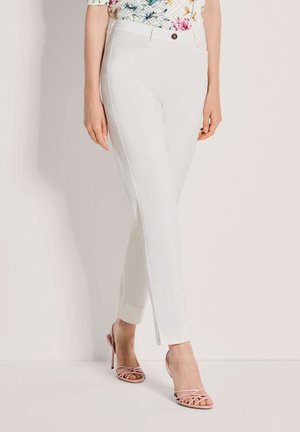 Witte, op maat gemaakte broek met een slanke pasvorm, voorzien van zijsplitten aan de zoom en een enkele knoop aan de voorkant. Gecombineerd met blushroze hakken met bandjes.