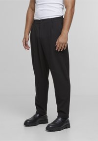 Svarte bukser med løs passform, med knappelukking og elastisk midjebånd, kombinert med svarte loafers. Glatt stofftekstur.