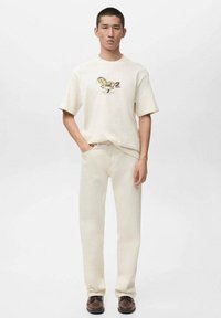 Kermanvärinen puuvillainen lyhythihainen t-paita, jossa on hevosen kuvio, yhdistetty vaaleanbeigeihin farkkuihin. Tummanruskeat kengät täydentävät asun.