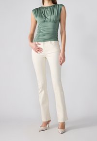 Grön, kortärmad, rynkad topp i kombination med ljusgrå, raka jeans och beige, spetsiga klackar. Slätt tyg och passform.