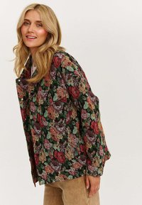 Kurtka w kwiecisty wzór z czarnym tłem, ozdobiona wielokolorowymi różami, z zapięciem na guziki i luźnym krojem. Teksturalny materiał dodaje wizualnego zainteresowania.
