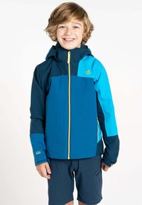 Blaue und türkisfarbene wasserdichte Jacke mit Kapuze, gelbem Reißverschluss und Logo. Kurze Ärmel und eine glatte Textur. Getragen mit navyblauen Shorts.