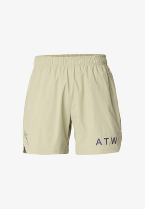 Junger Mann steht frontal, trägt ein weißes übergroßes T-Shirt mit Text auf der Brust, hellgrüne Shorts mit schwarzen Buchstaben, schwarze Socken und beige Turnschuhe.