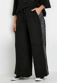 Czarne spodnie szerokie z elastycznym pasem, z boku z panelem w leopardzi wzór. Miękka tekstura, połączone z czarnymi tenisówkami.