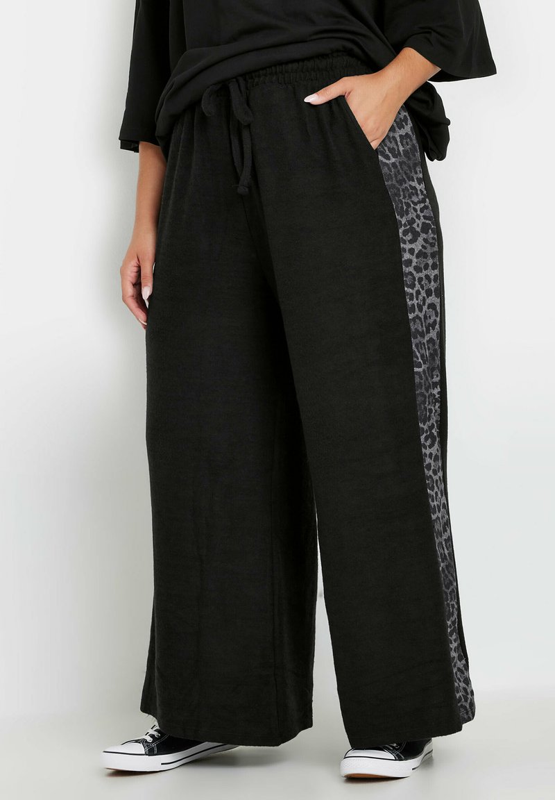 Czarne spodnie szerokie z elastycznym pasem, z boku z panelem w leopardzi wzór. Miękka tekstura, połączone z czarnymi tenisówkami.
