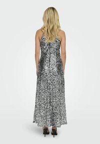 Robe de soirée en sequins argentés avec une jupe fluide et des bretelles spaghetti réglables, fermeture éclair au dos et un corsage ajusté. Portée avec des talons noirs.