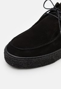 Scarpa in suede nera con punta arrotondata, suola in gomma texturizzata e cuciture a contrasto. I lacci sono legati sul lato superiore.