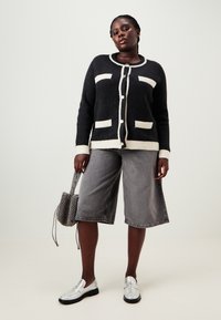 Μαύρος και κρέμα ζακέτα με τρεις τσέπες, κουμπιά μπροστά και ριμπ μανσέτες. Συνδυασμένη με γκρι τζιν σορτς και ασημένια μοκασίνια.