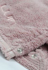 Rosa fleecefilt med texturerad, fluffig yta. Utrustad med metalltryckknappar och broderad logotyp längs kanten.