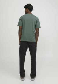 T-shirt vert à manches courtes en coton, avec un col rond. Associé à un pantalon en denim noir et des baskets grises. Design minimaliste.