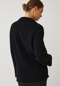 Sort strikket cardigan med en afslappet pasform, bred krave og ribbet struktur, der har sænkede skuldre og sideslids for nem bevægelse.