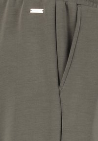 Donkergroene lichtgewicht broek met een gladde textuur, elastische tailleband, koord, zijzakken en een klein zilveren accentlabel.