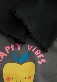 Tissu gris avec un motif de pomme en jaune et des feuilles bleues. "HAPPY VIBES" en lettres roses. Tissu noir à côtes avec des bords effilochés.