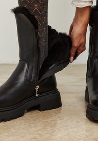 Botas de cuero negro con un acabado texturizado, que cuentan con un forro de piel sintética y una cremallera expuesta para una fácil colocación. Suelas de goma gruesas.