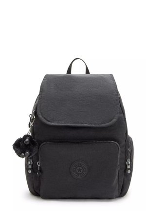 Black nylon backpack with a flap closure, front zip pocket, and decorative pom-pom keychain. Features a circular brand logo on the front.