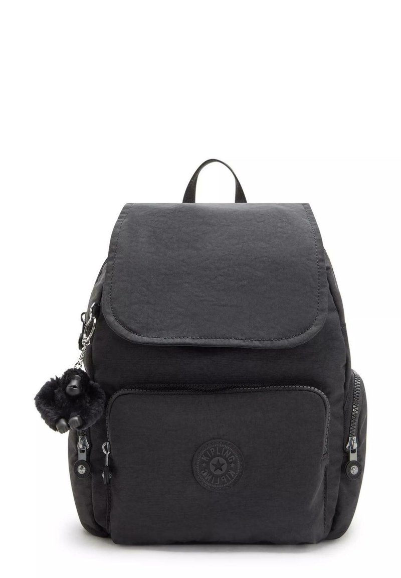 Black nylon backpack with a flap closure, front zip pocket, and decorative pom-pom keychain. Features a circular brand logo on the front.