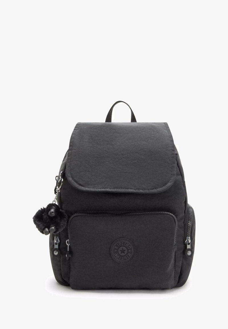 Černý nylonový batoh s klopovým víkem, přední kapsou na zip a ozdobným klíčenkou s bambulkou. Na přední straně má kulatou značkovou nálepku.