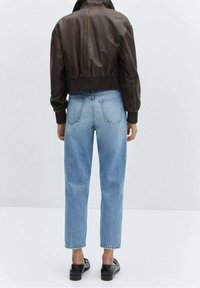 Bruine leren cropped jack, met ribbels aan de manchetten en zoom. Lichtblauwe hoge taille rechte jeans met een vervaagde afwerking en zwarte schoenen.
