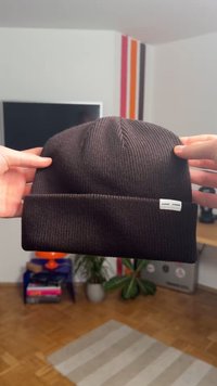 Berretto a maglia marrone scuro con texture a coste e risvolto. Presenta una piccola etichetta bianca del marchio sul risvolto.